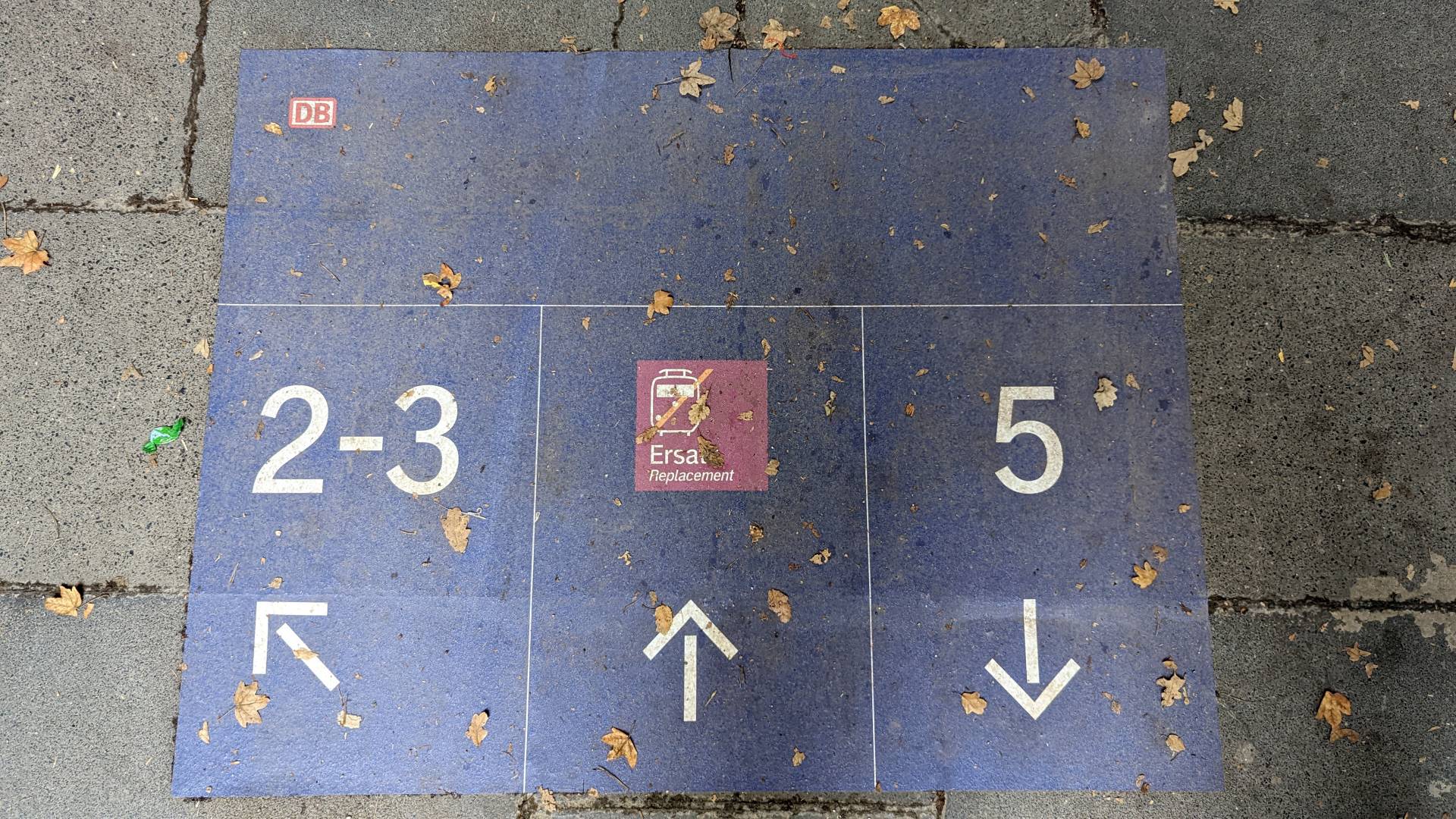 Ein blaues Schild auf dem Boden mit den Hinweisen zu den Gleisen und der Richtung, in der sich die jeweiligen Gleise befinden.